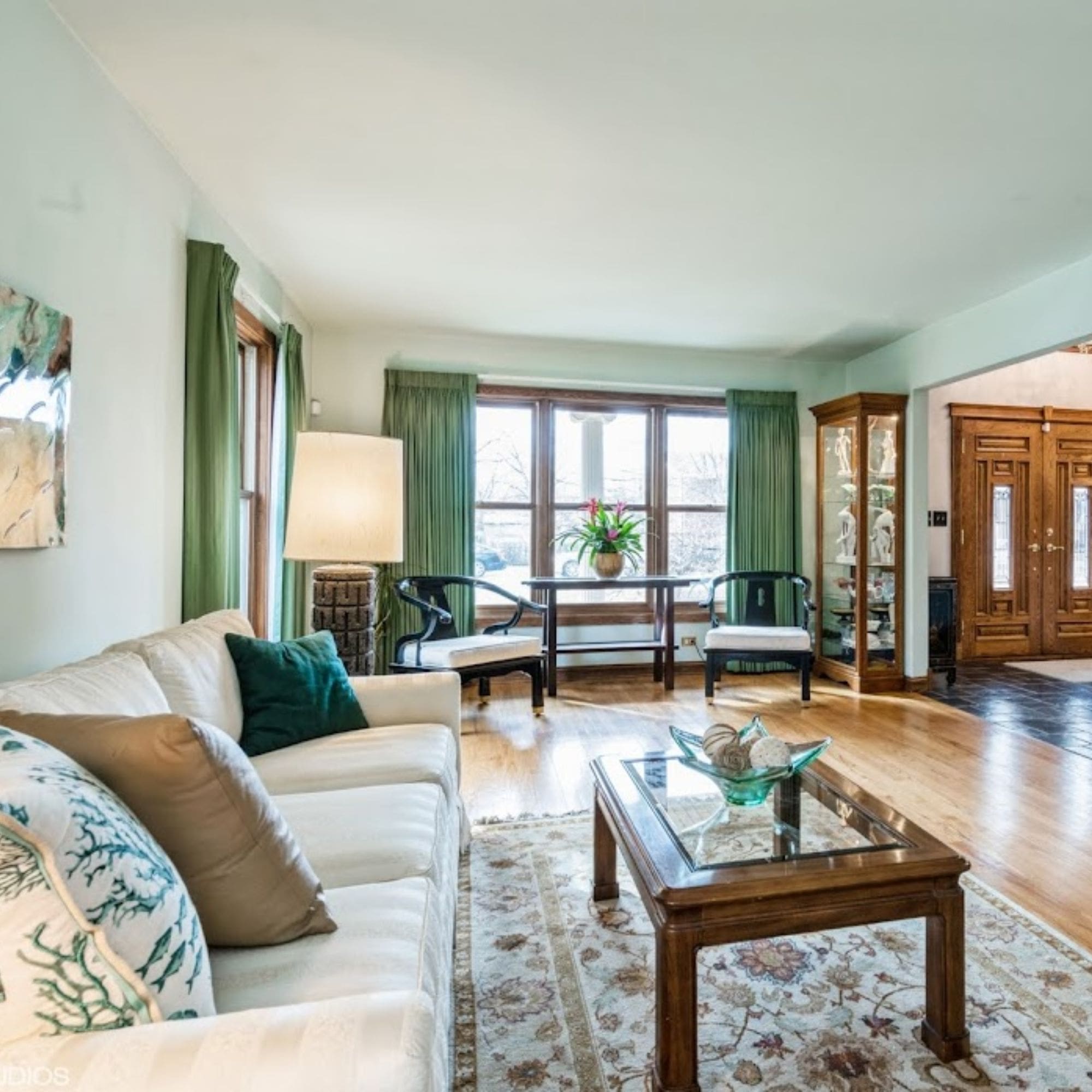 A stylish home staged living room featuring vibrant green curtains and elegant hardwood floors.