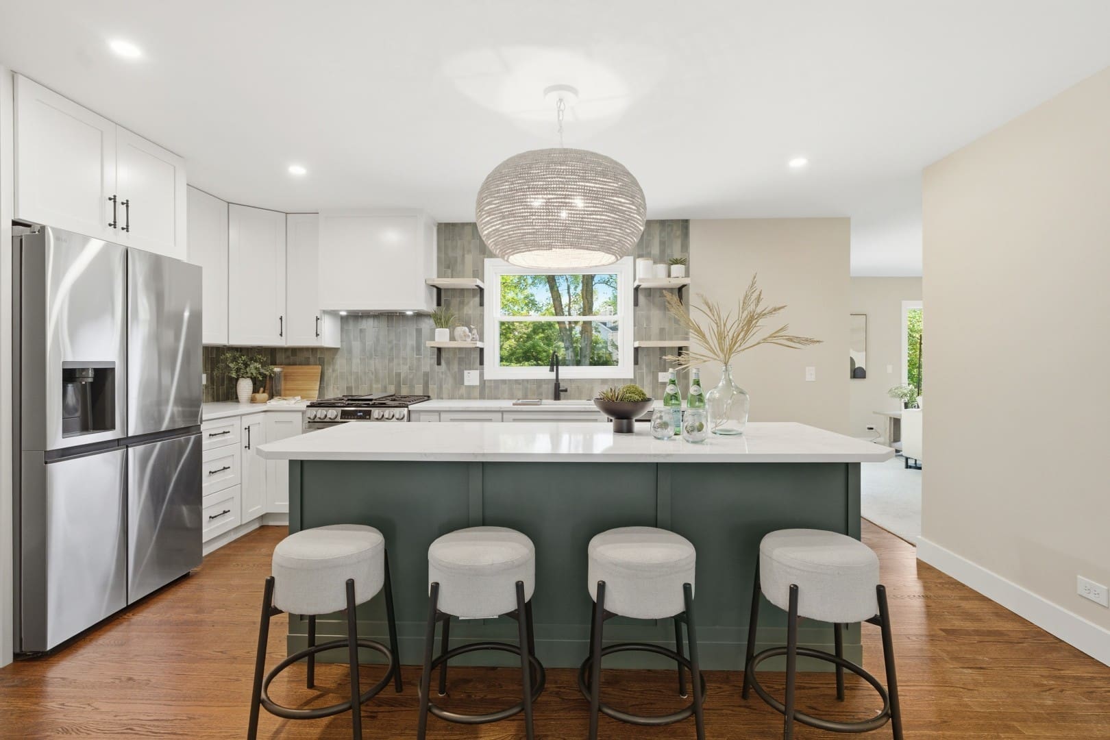 HD_1783636955377_006_kitchen_010_1342_Winchester_Ct_Large Modern kitchen with white upper cabinets, a dark sage green island with four barstools, stainless steel appliances, and a spherical woven pendant light.