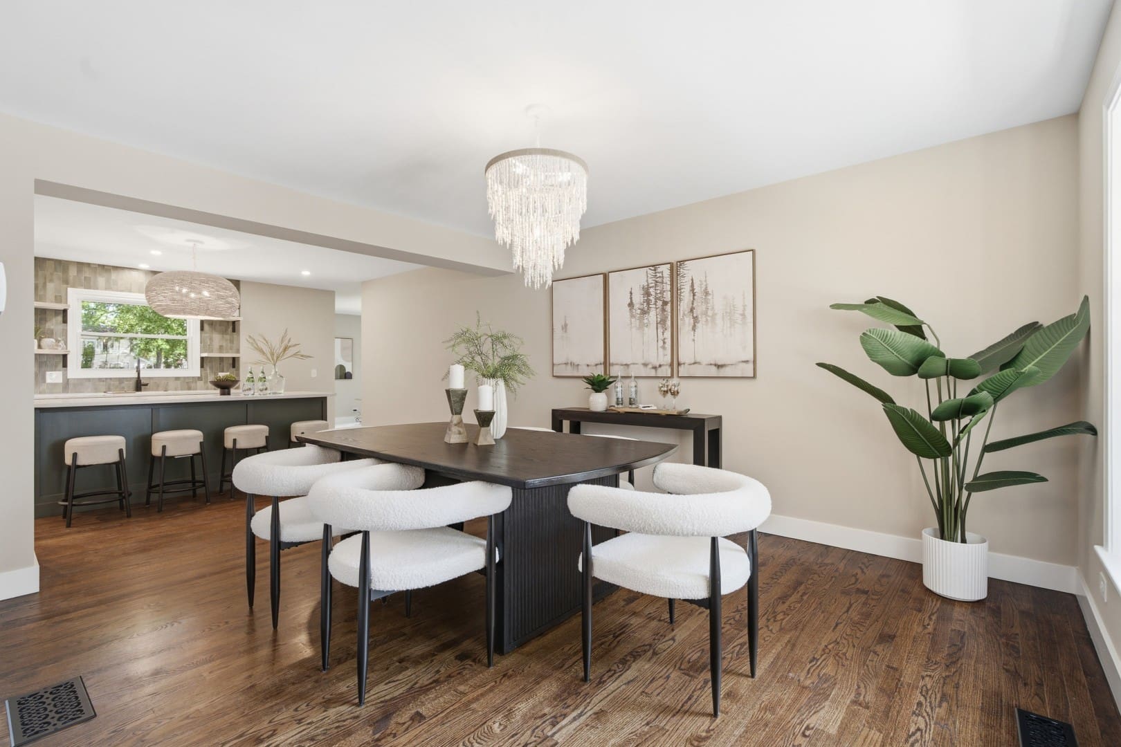 HD_1783636955615_008_dining_012_1342_Winchester_Ct_Large (1) Modern dining room featuring a dark wood dining table with plush white bouclé chairs, a beaded chandelier, and an open view into the adjacent kitchen.